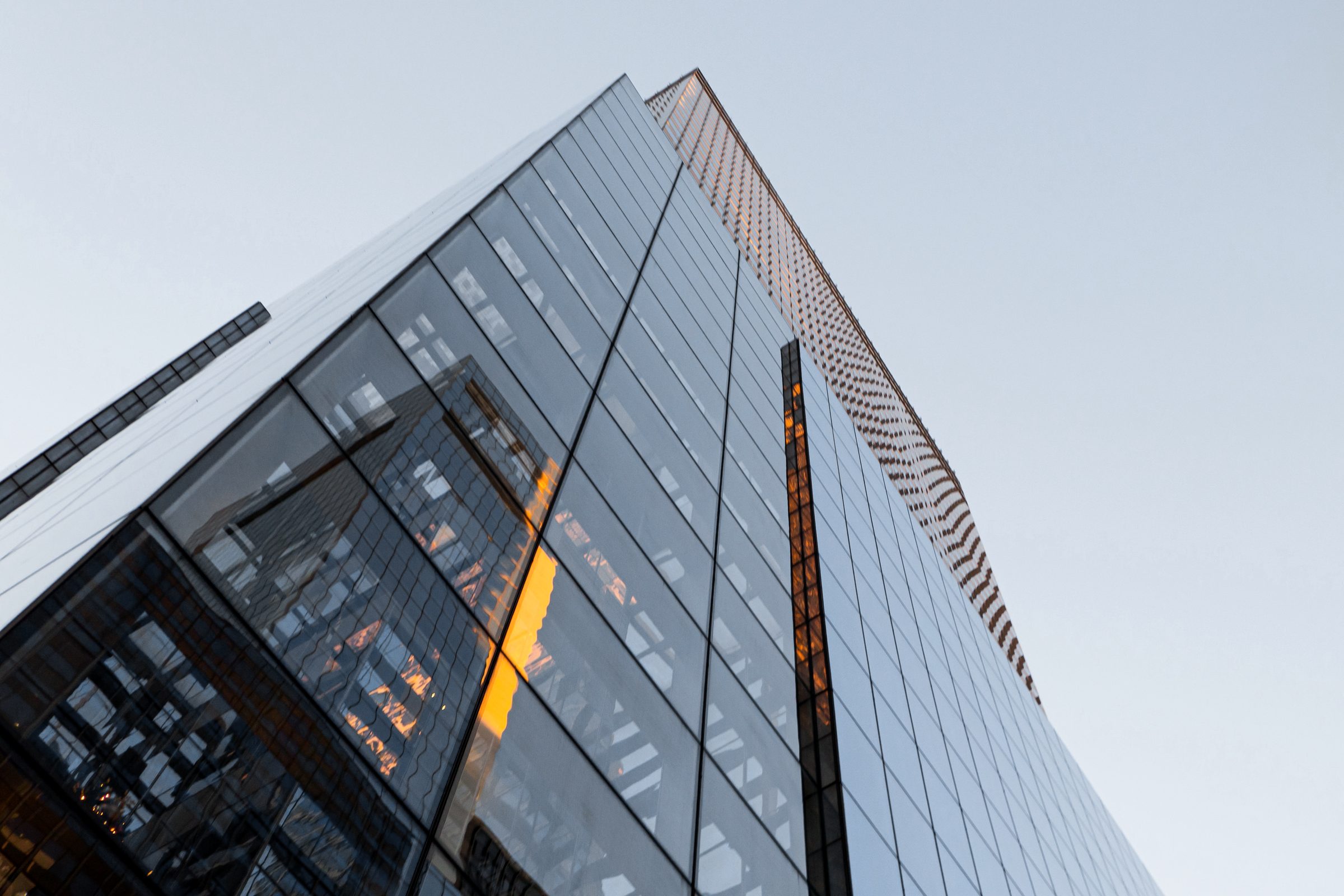 Looking up the glass curtain wall of a modern commercial tower catching warm light