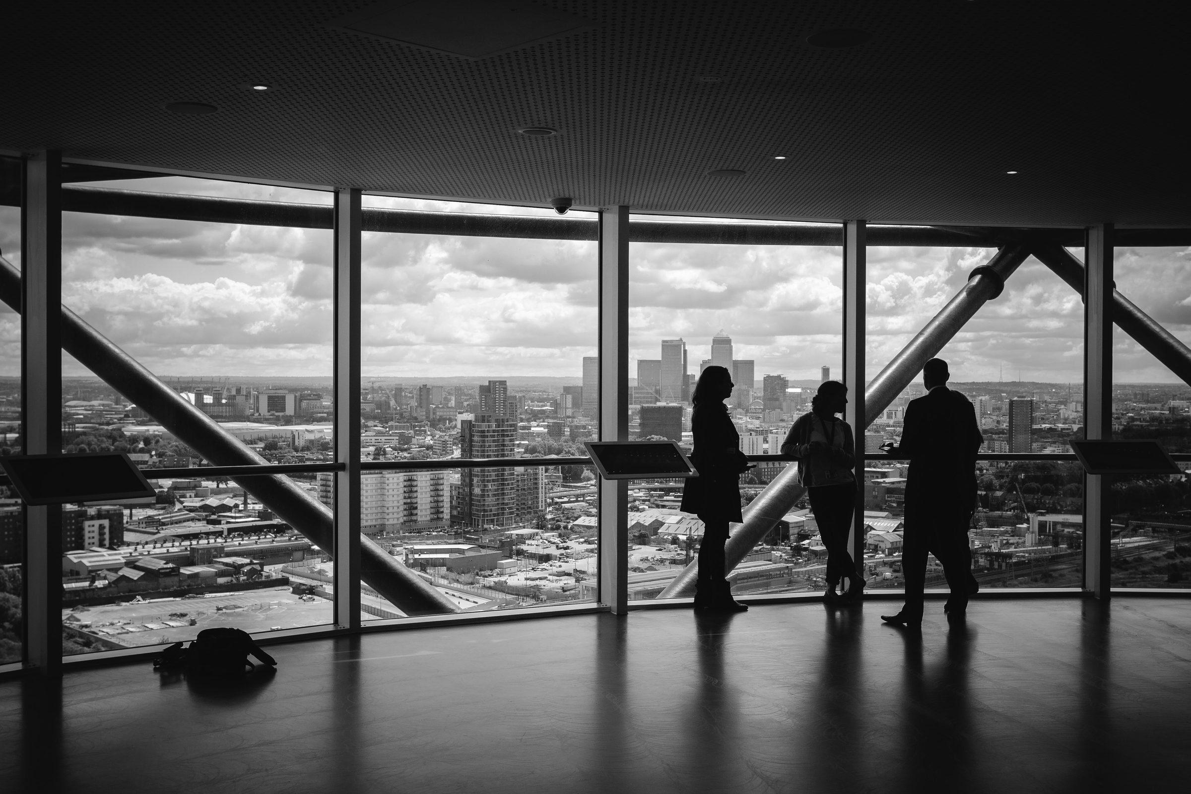 Black-and-white view of three silhouetted figures at a glass office wall overlooking a city